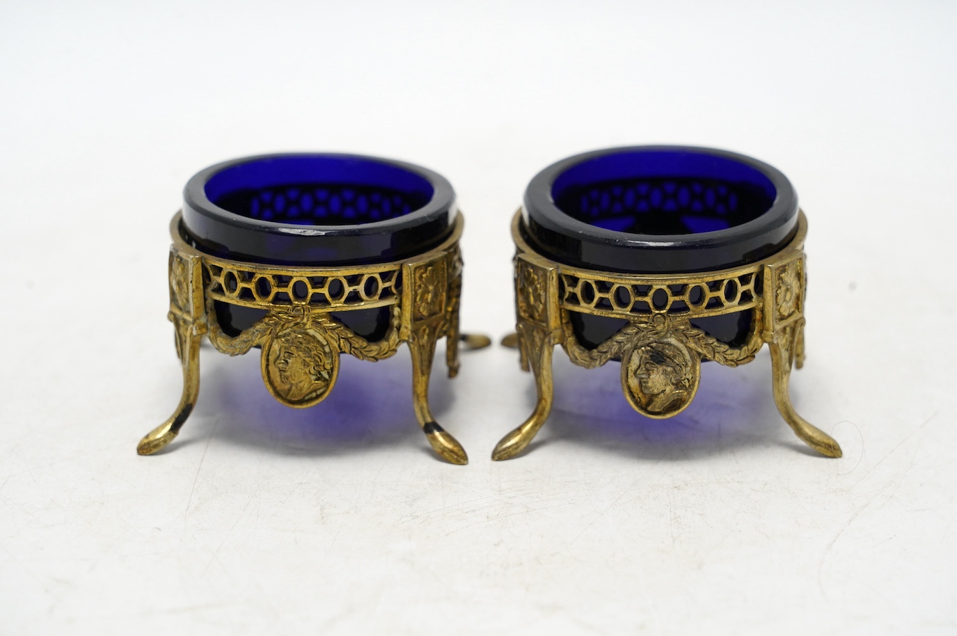 A pair of late 19th/early 20th century continental pierced gilt white metal oval salts, with blue glass liners, 69mm. Condition - fair